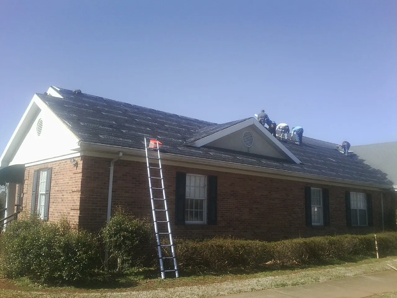 Crew tearing shingles off a brick ranch roof with a ladder set — Metal Roof Repair work by our crew in Montpelier